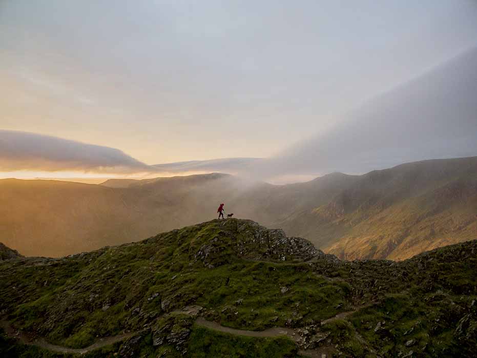 dog and man walking on cliff edge at sunrise